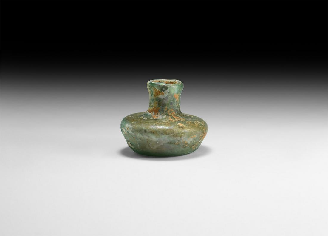 Roman Green Glass Vessel: 4th-5th century AD. A squat iridescent green glass bottle with dimple base, broad shoulder and low neck with applied rim. Cf. Whitehouse, D. Roman Glass in the Corning Museum of Glass, vol.1, New York