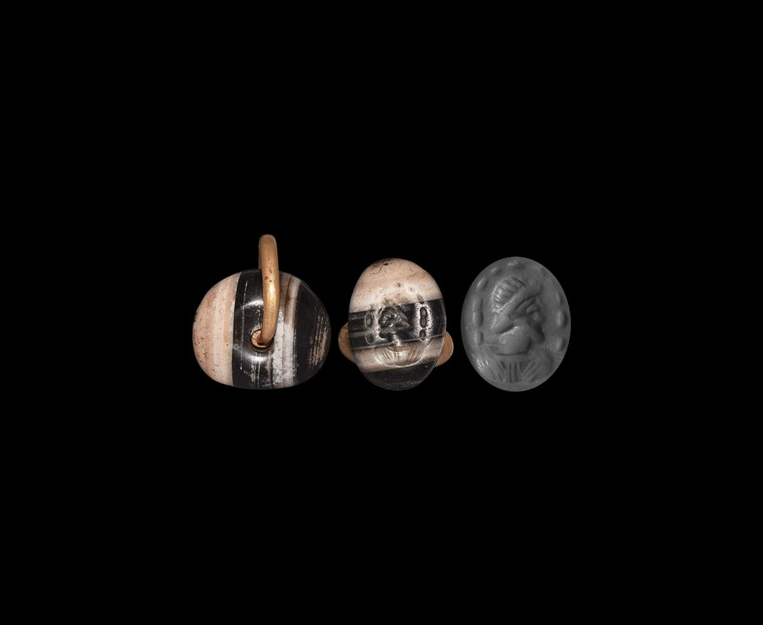 Sassanian Stamp Seal with Gold Loop: 3rd-7th century AD. A plano-convex banded agate stamp seal pierced to accept a gold suspension loop, intaglio bearded profile bust with arc of pellets around. Accompanied by a museum-quality impressio
