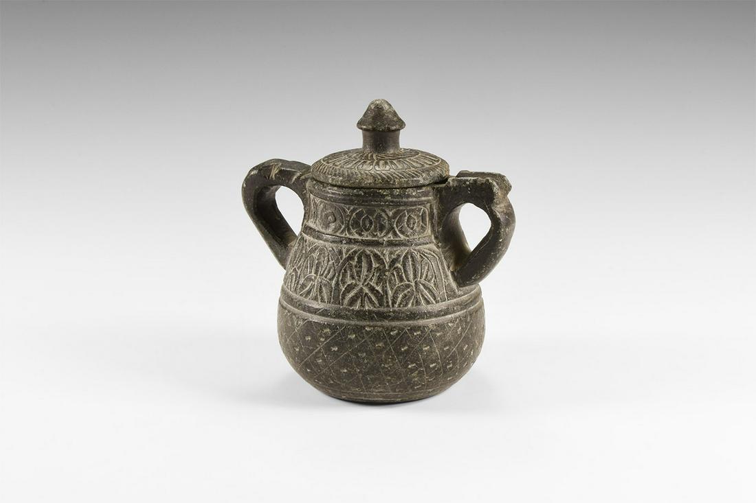 Islamic Carved Aromatic Oil Jar: 10th-12th century AD. A carved chlorite pot with separate lid with petal pattern around the rim; pot with band of rosettes at the neck and palmettes at the body, both separated by a collar; two handle
