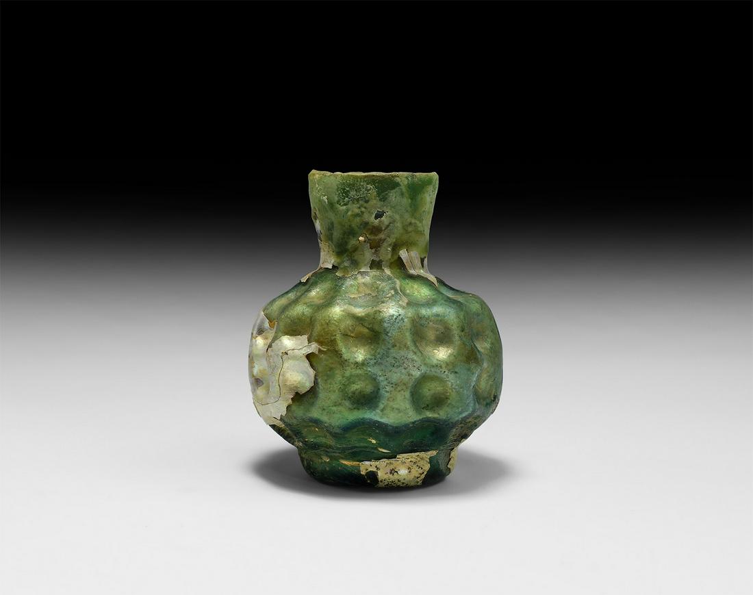 Roman Dimpled Glass Vessel: 2nd-3rd century AD. A squat iridescent green glass jar with annular base, three rows of dimples to the body and shoulder, slightly flared neck. 54 grams, 73.5mm (3"). From an important central London 