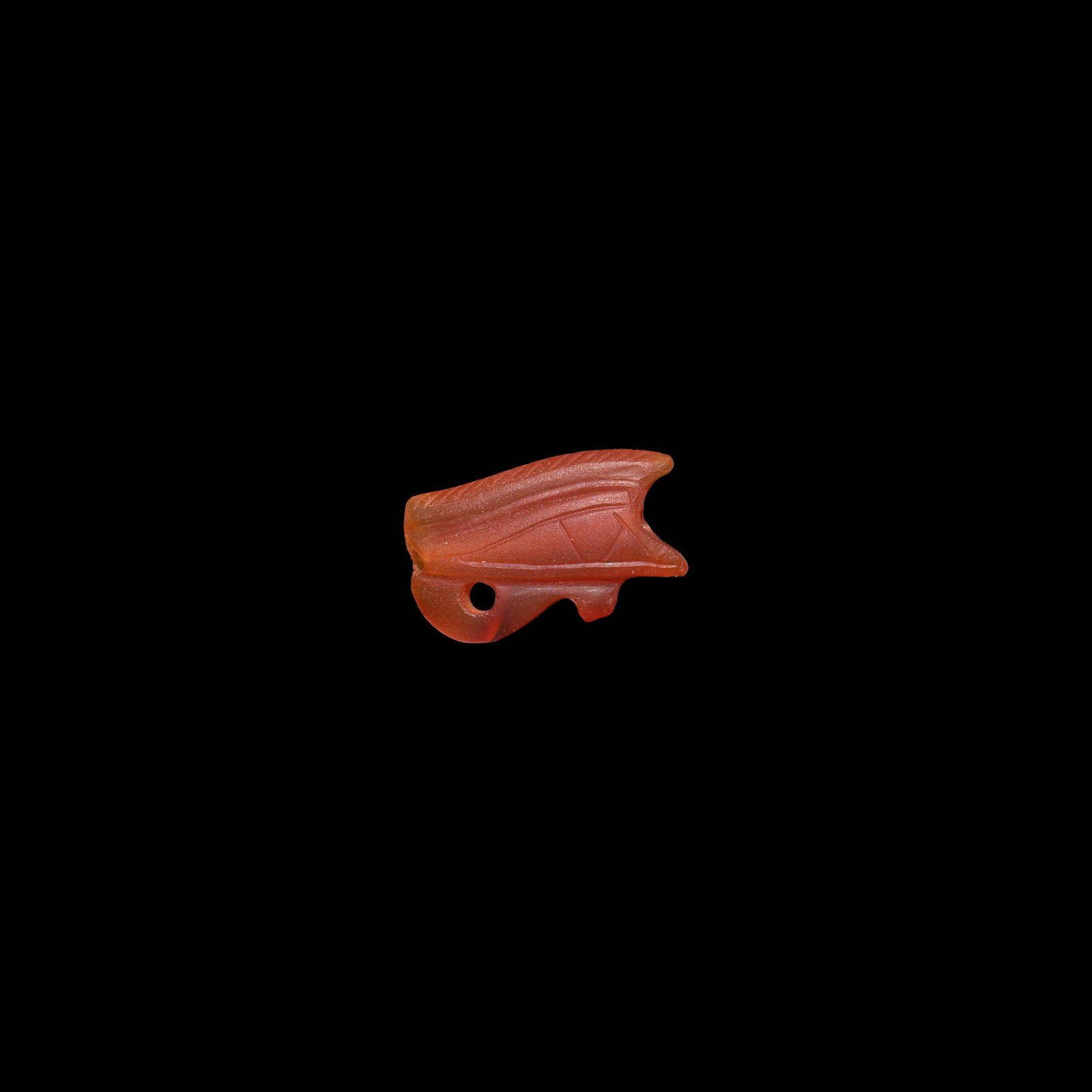 Egyptian Carnelian Wedjat Eye Amulet: New Kingdom, 1550-1070 BC. A carved bifacial red carnelian wedjat eye amulet with large incised eye detailing on a raised median band, short teardrop, keeled eyebrow with hatched detailing above; pier