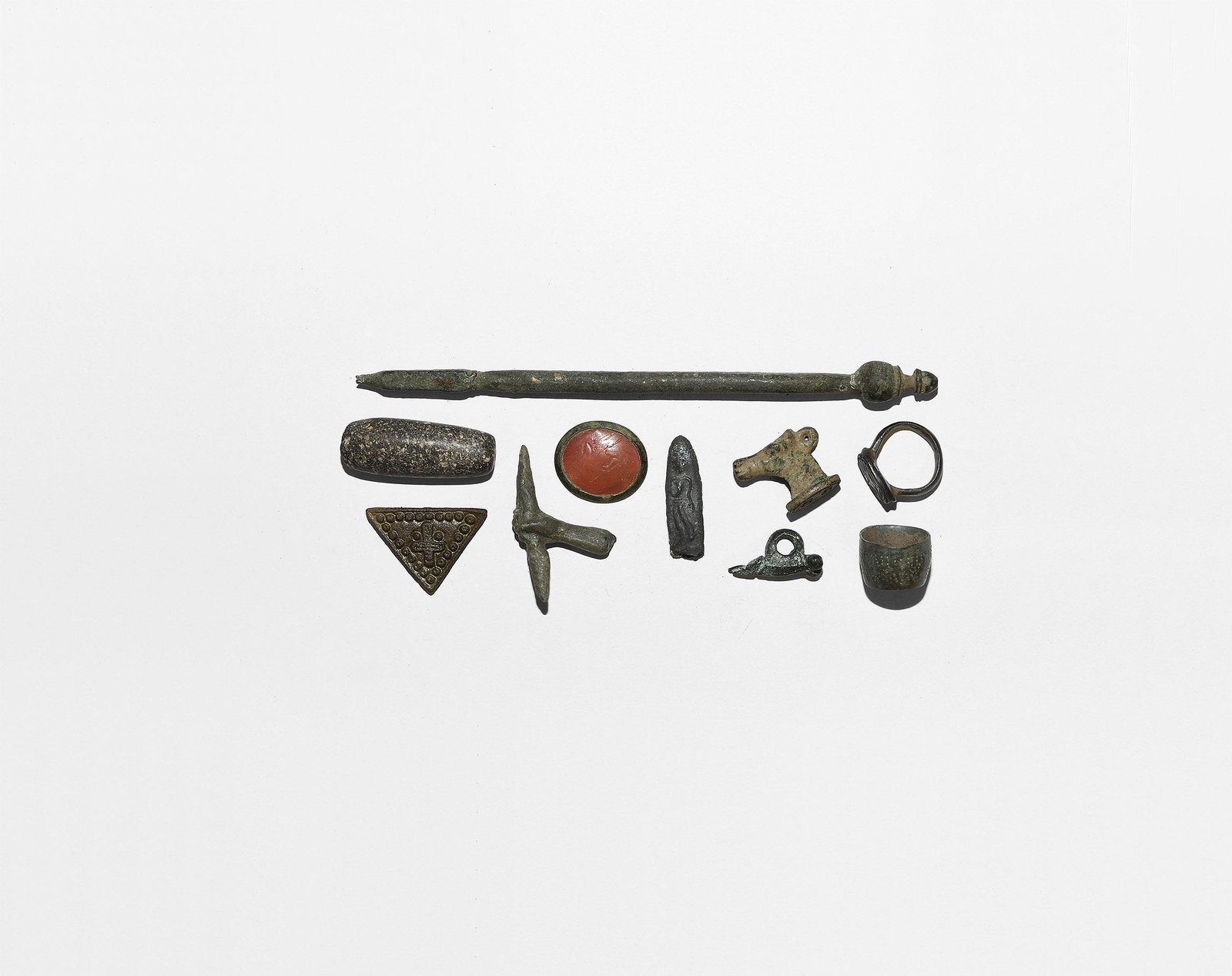 Roman and Other Artefact Group: 2nd millennium BC-15th century AD. A mixed group of artefacts comprising: a bronze phallic pendant; a bronze statue hand holding a thunderbolt; a bronze triangular mount with cross; a carnelian intagl