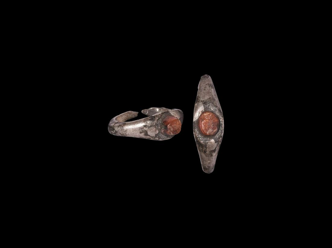 Roman Silver Ring with Frond Gemstone: 3rd century AD. A silver finger ring comprising a D-section hoop with keeled shoulders, ellipsoid bezel with inset carnelian stud, intaglio frond motif. 4.04 grams, 26mm overall, 18.5mm internal diame