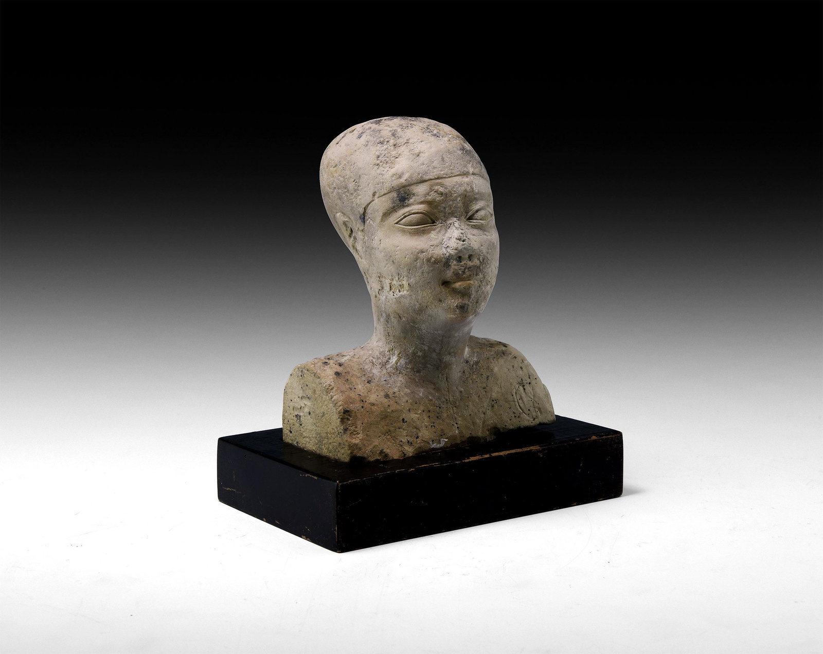 Egyptian Head of a Priest: Ptolemaic Period, 332-30 BC. A carved limestone bust of a priest with close-fitting cap, serene expression with prominent lentoid eyes, small nose and full lips; collector's note and old auction stick