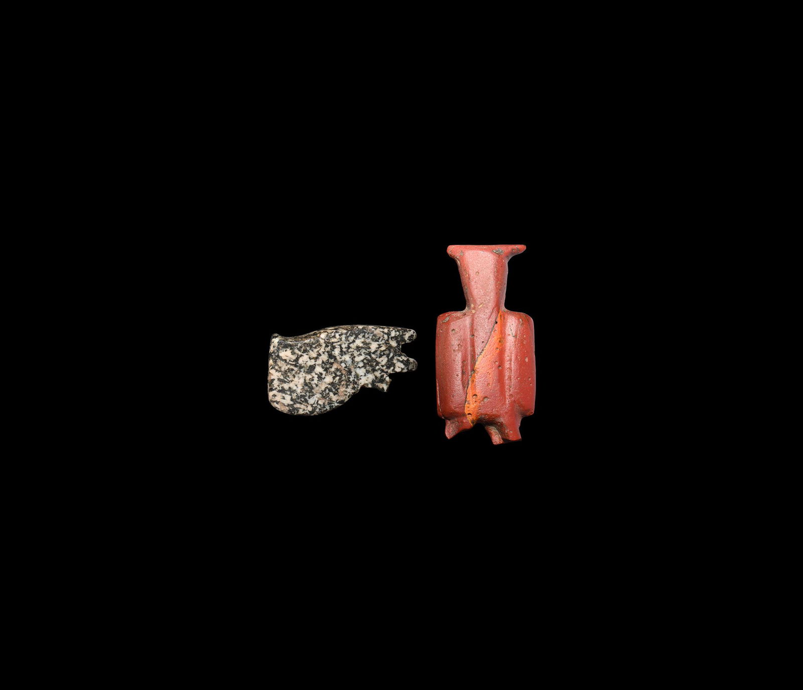 Egyptian Amulet Group: Late Period, 664-332 BC. A pair of amulets comprising: a granite wedjat eye, pierced for suspension; a red glass tyet, girdle of Isis, amulet, loop absent. 22.1 grams total, 34-46mm (1 1/4 - 1 3/4").