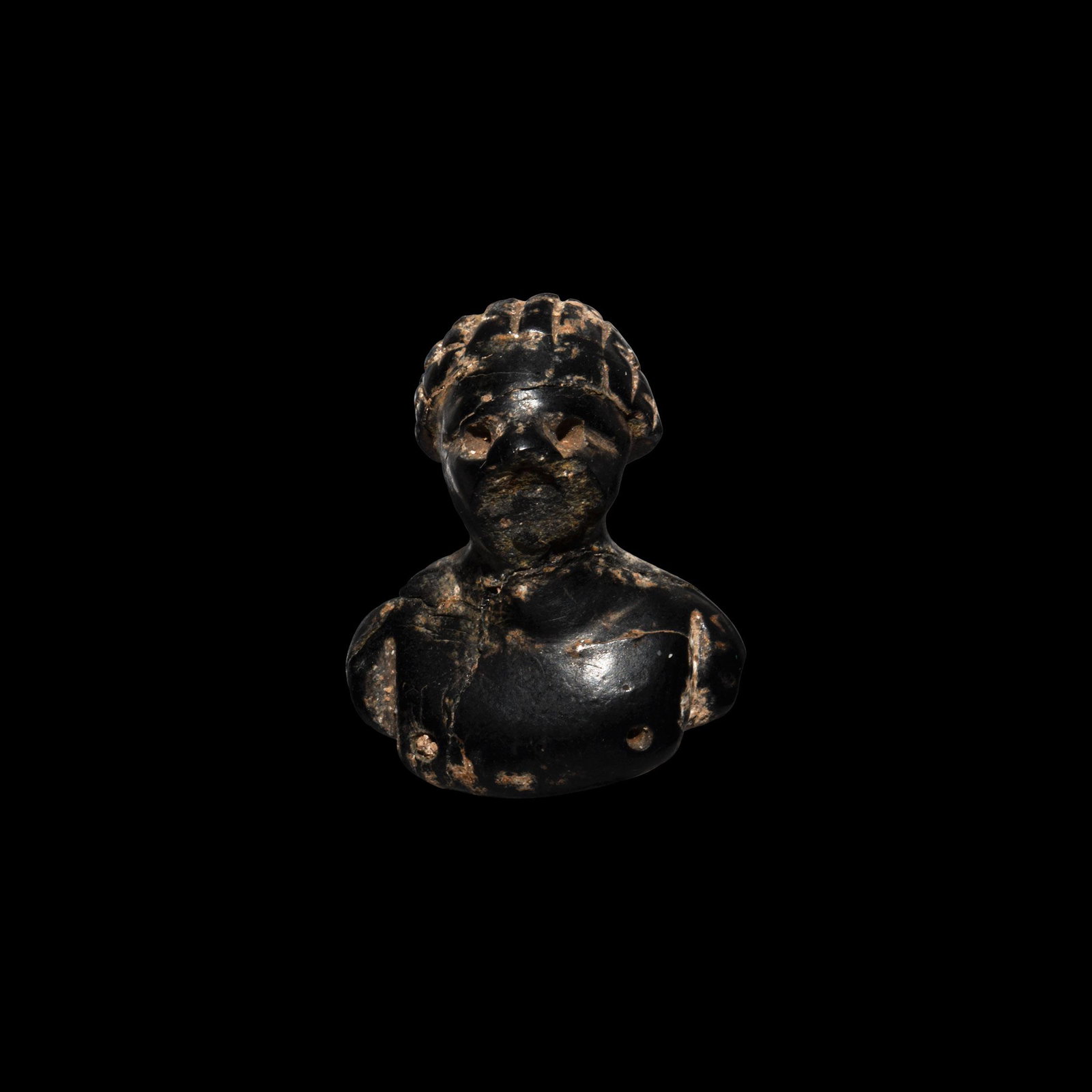 Hellenistic Jet Nubian Bust Applique: 6th-4th century BC. A black jet applique depicting bust of a nude mail with reticulated hair, recessed eyes to accept inserts. 2.7 grams, 25mm (1"). From the property of a London gentleman; thence by 