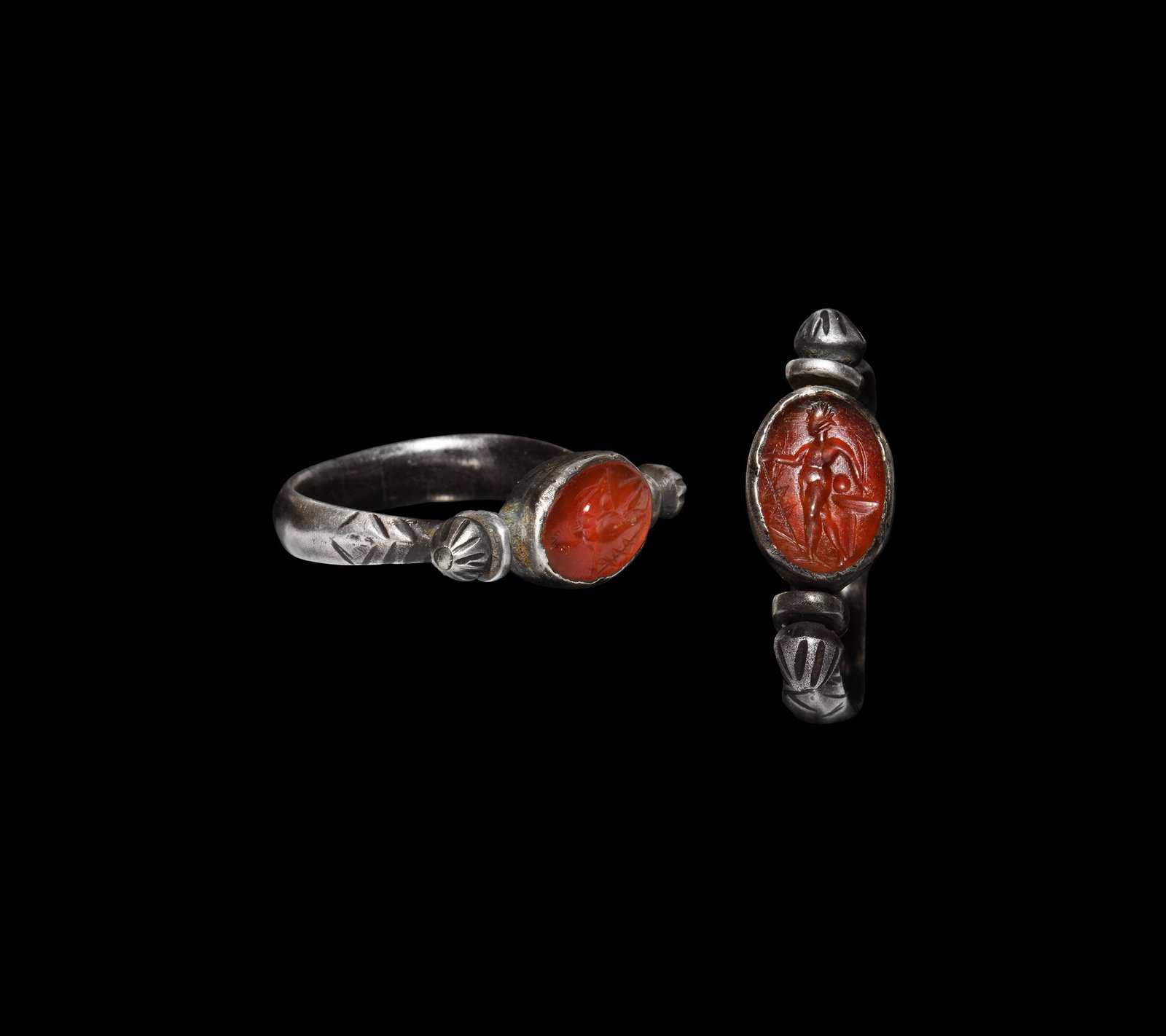 Roman Silver Ring with Asclepius Gemstone: 1st century BC-1st century AD. A silver swivel ring with keeled hoop and hatched shoulders, swivel bezel inset with carnelian intaglio engraved with Asclepius holding his snake-entwined staff in his r