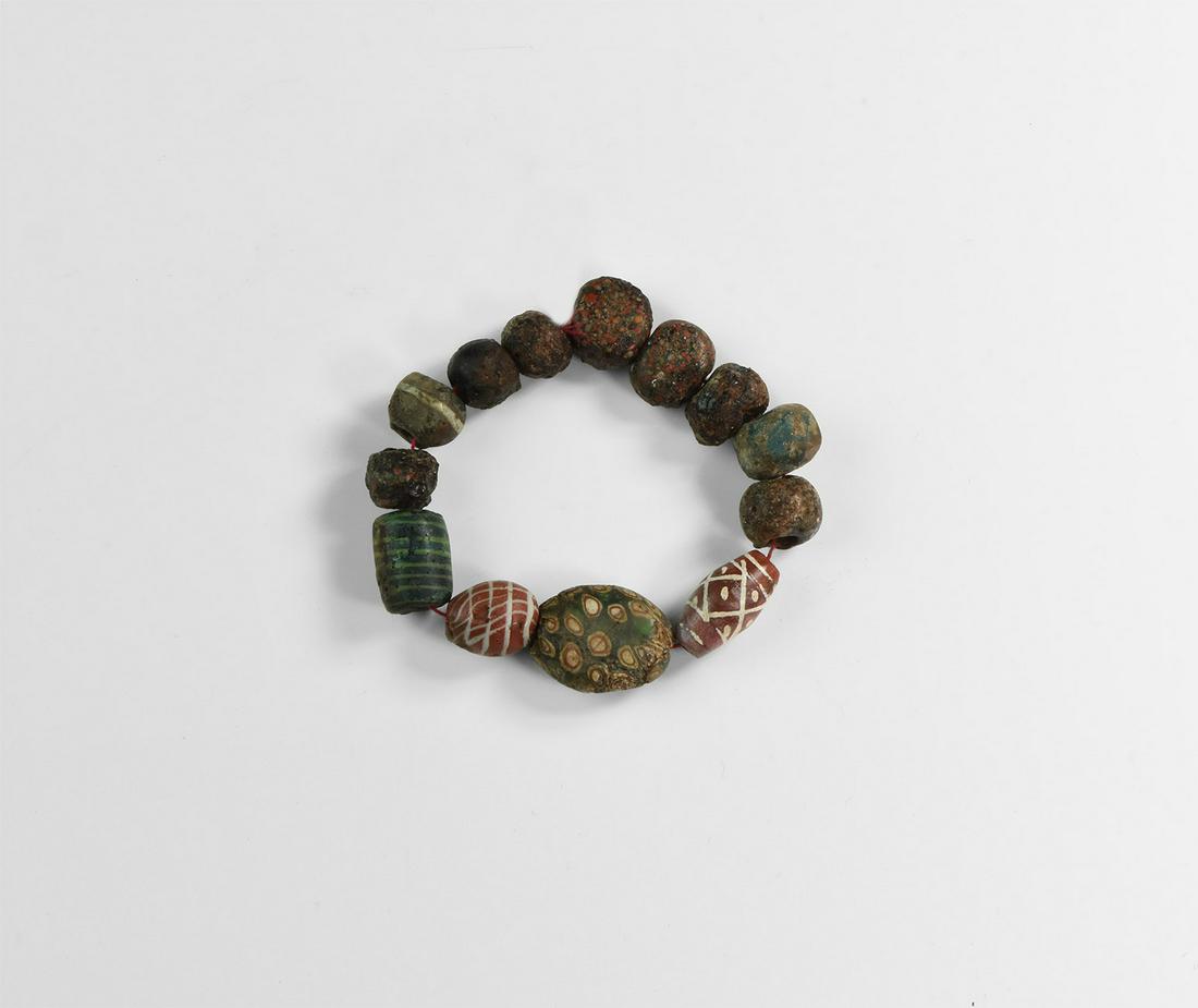 Roman Glass Bead Group: 1st-3rd century AD and later. A restrung group of mosaic glass beads including a tabular millefiori bead; lamp- and furnace wound glass beads and a fusiform carnelian bead with engraved design. 48 gra
