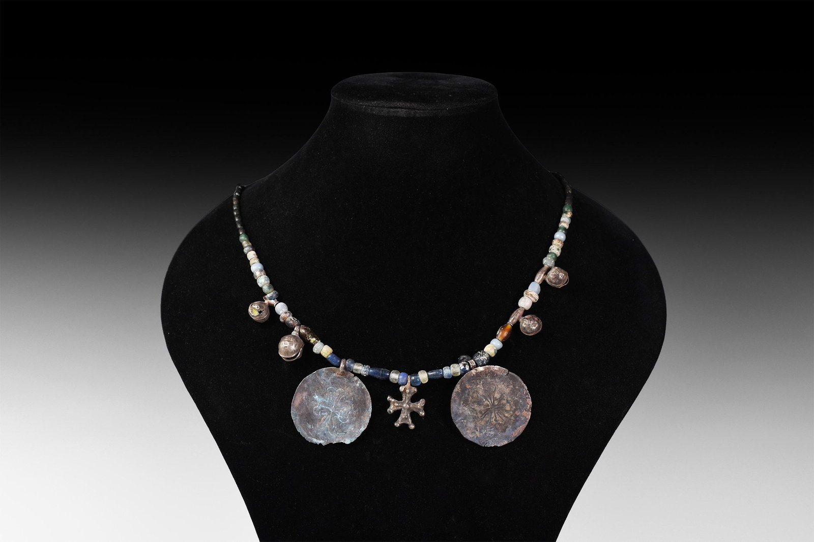 Byzantine Glass Bead Necklace with Silver Pendants: 10th-12th century AD. A restrung necklace composed of graduated glass beads with four silver bell pendants, a central cross pendant and two flanking large discoid pendants with engraved equal-armed cr