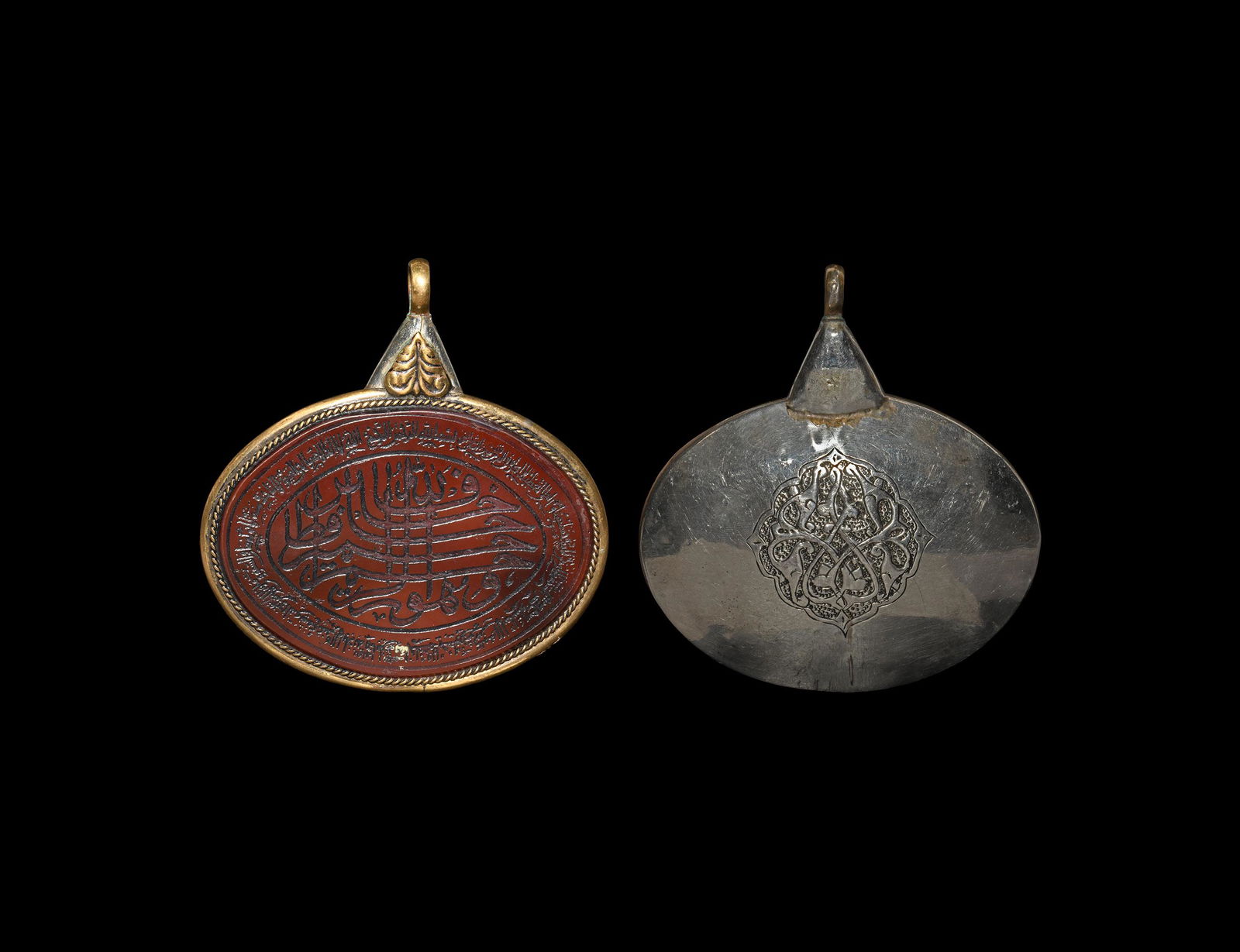 Islamic Calligraphic Gemstone in Silver Pendant: 20th century AD. A large oval silver and brass pendant with ropework border, applied leaf motif below the suspension loop, inset with jasper(?) intaglio with engraved calligraphic text border surround