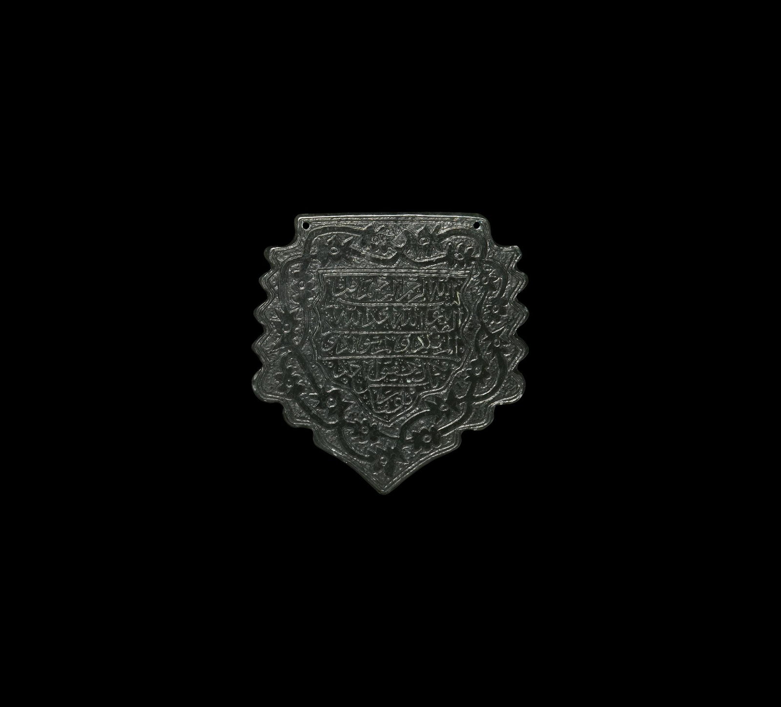 Islamic Calligraphic Gemstone Plaque: 20th century AD. A heater-shaped agate plaque with running tendrils reserved on a hatched field, central panel with five lines of calligraphic text. 15.5 grams, 52mm (2"). From the family collection o