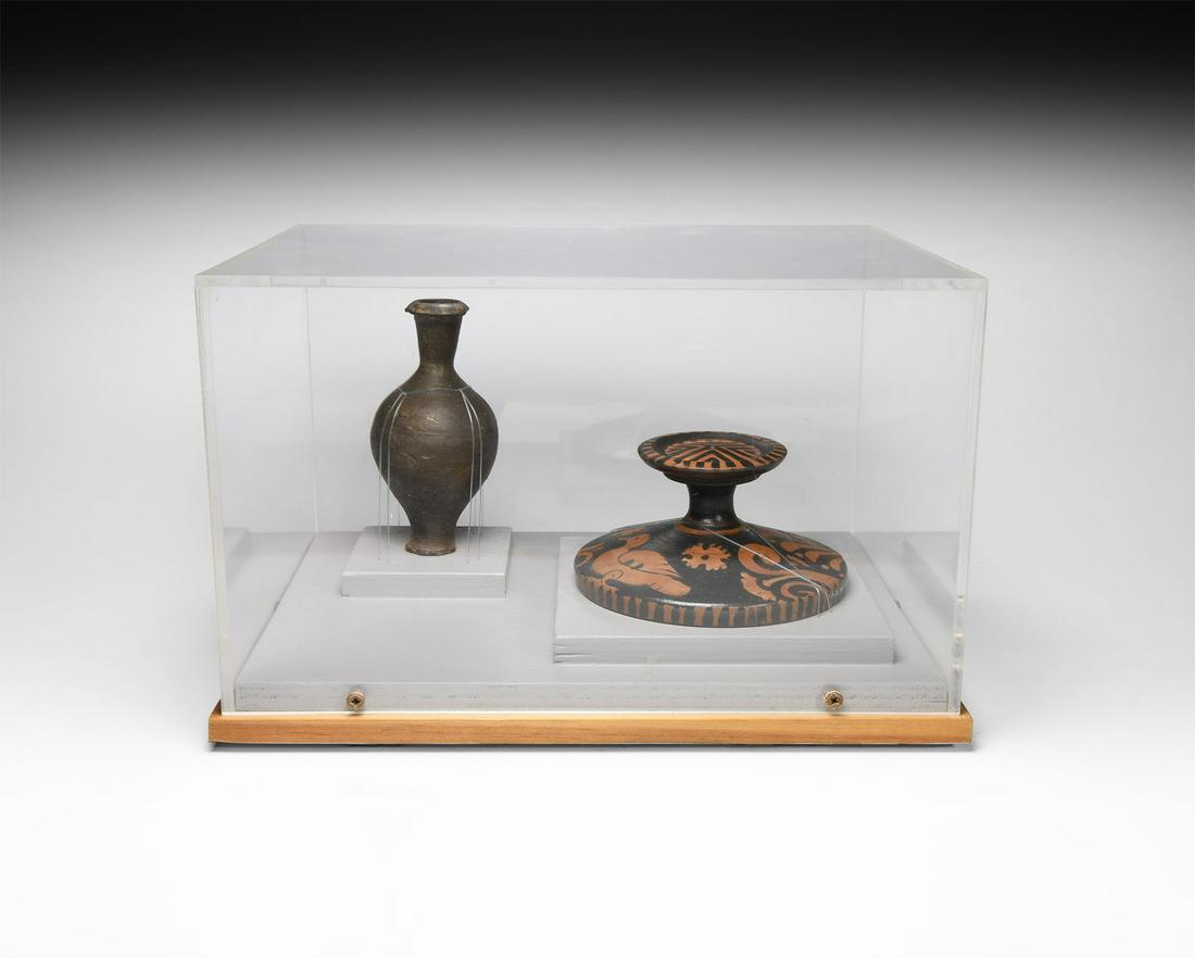 Greek Red Figure Lekanis Lid: 5th-3rd century BC. A red figure ware lekanis lid decorated with a duck, displayed with a perfume bottle in grey terracotta; mounted on custom-made stands within a custom-made perspex display case. 91