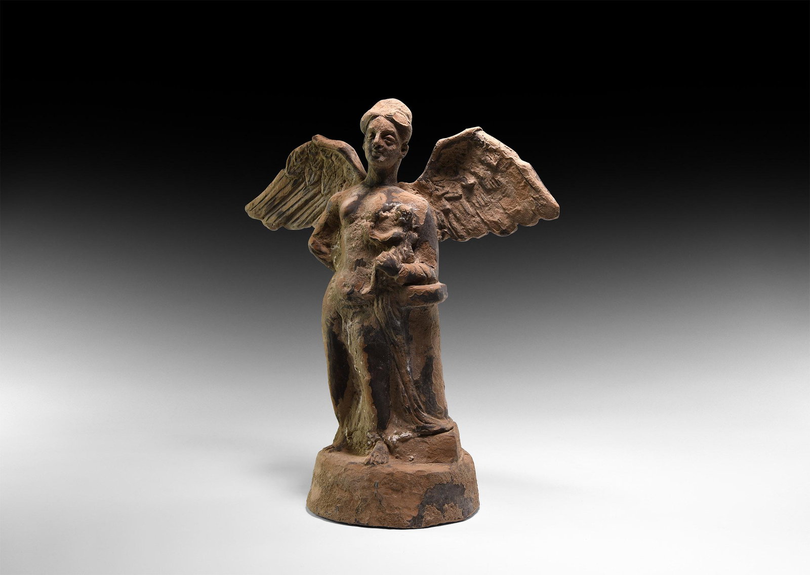Greek Winged Tanagra Figure: 4th-2nd century BC. A hollow-formed moulded ceramic figurine of Tanagra type with rectangular slot to the reverse; standing female with wings extended suckling a baby in the crook of her left arm. 740