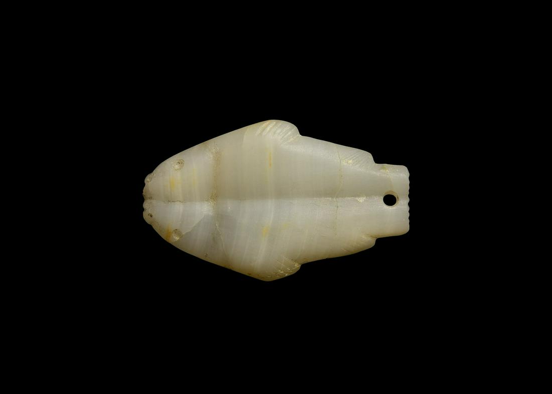Double Fish Amulet: 2nd-1st millennium BC. A carved alabaster amulet of a pair of fish conjoined at the abdomen, drilled eyes and nostrils, pierced through the tail for suspension. 30 grams, 63mm (2 1/2"). Ex private Lon