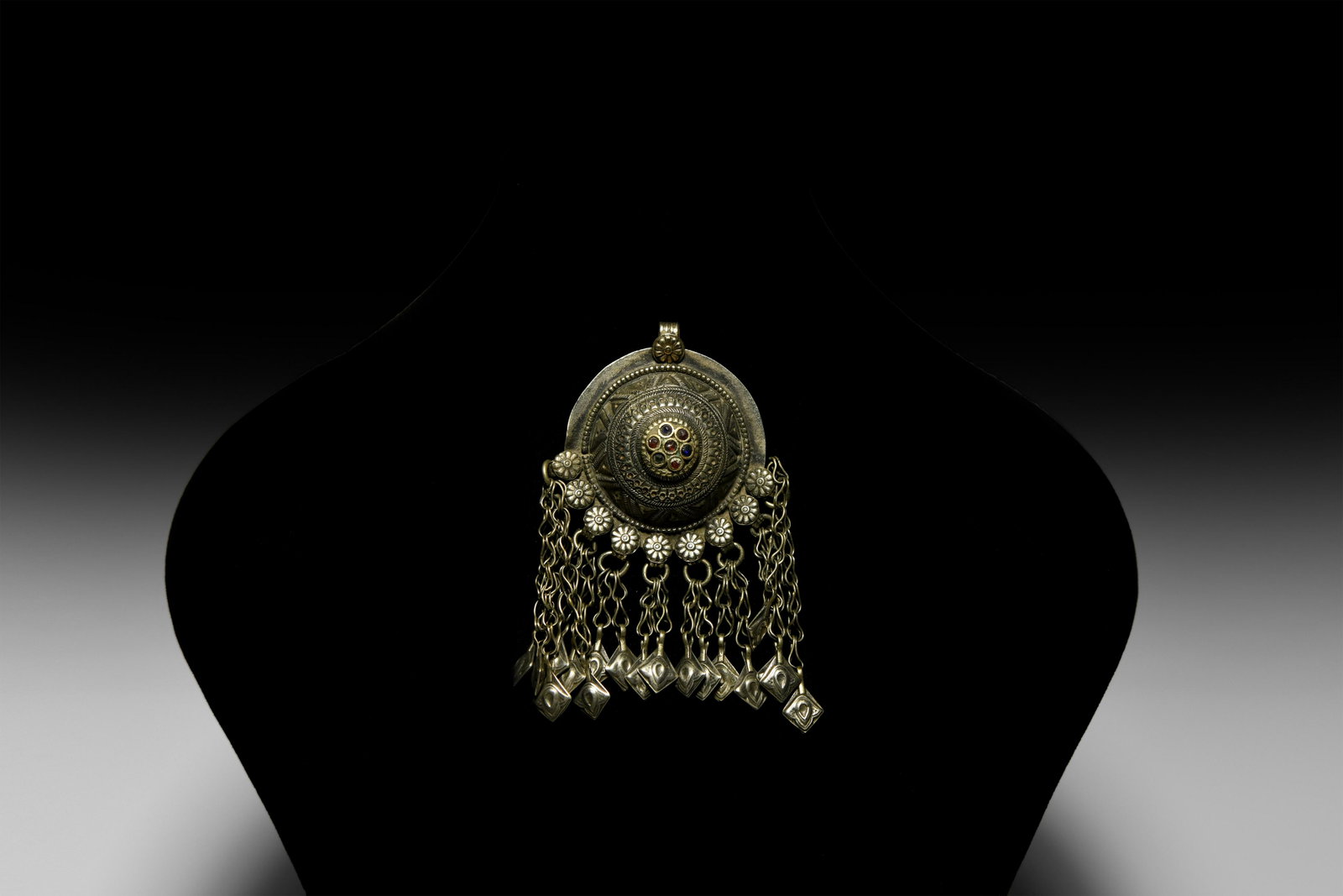 Turkoman Tribal Domed Discoid Pendant: 20th century AD. A white metal pendant with domed decorative centre set with glass cabochons, nine rosettes below with chains and lozenge-shaped pendants. 59 grams, 11.3cm (4 1/2"). Property of a Lond