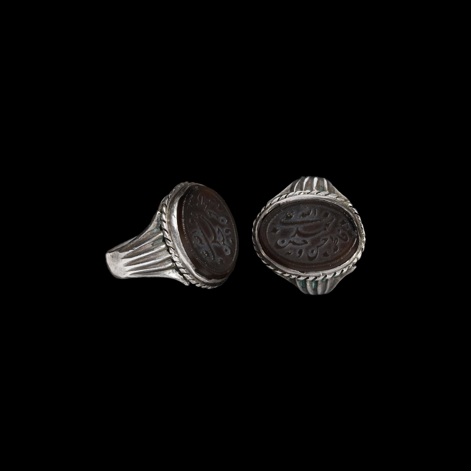 Islamic Silver Ring with Inscribed Gemstone: 19th-early 20th century AD. A silver finger ring with ribbing to the flared shoulders, ropework collar to the cell, inset (older?) carnelian cloison with reserved text on a frosted field 'Allah, Moham