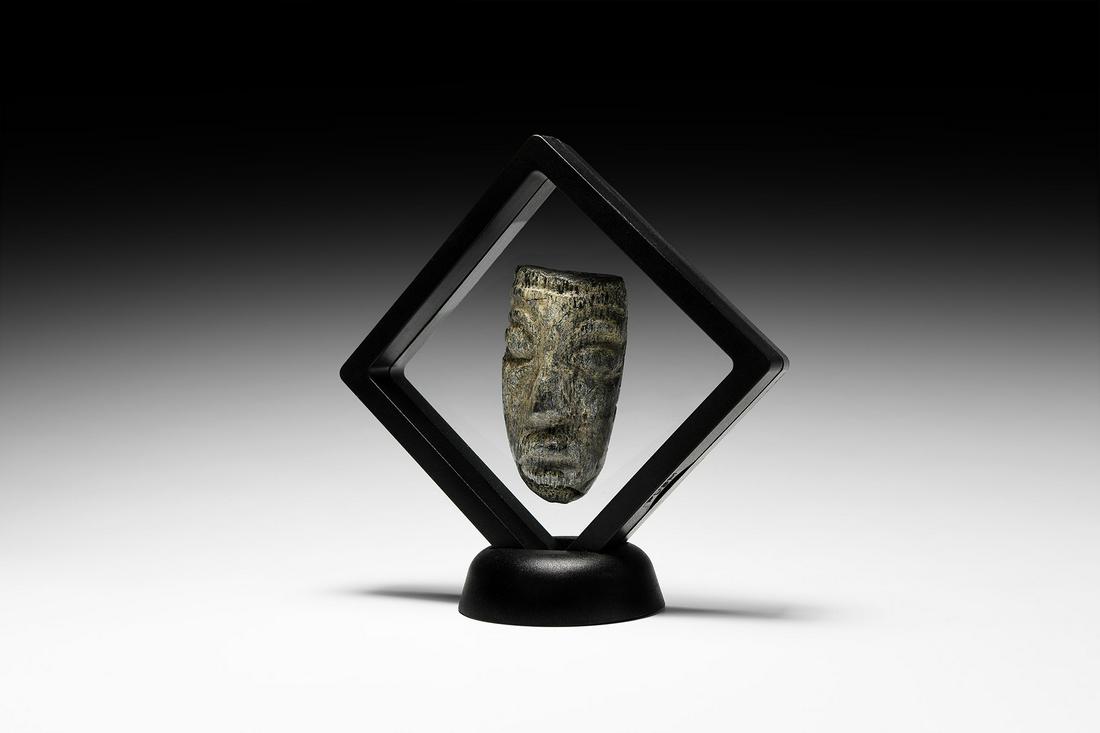 Carved Mastodon Tusk Face: Pliocene Period, 5.2-2.5 million years BP. A fossil mastodon tusk with a later carving depicting an elongated human face with prominent eyes, nose and mouth; mounted in a custom-made display frame. 91