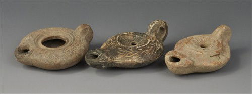 Roman Oil Lamps: Circa 1st century AD. A mixed group of oil lamps comprising: a small example with orange-red surface, decorated with roundels and plant motifs; a low, wide lamp with laurel-leaf design round the centr