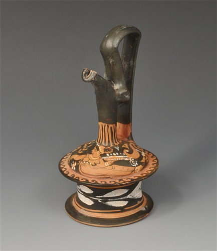 Greek - Apulian Figural Painted Epichyses: Circa 350 BC. An Apulian Gnathian ware epichyses enlivened with crimson, ochre and white slip; with rays on the neck, the shoulder showing a lady of fashion lying, adorned with a necklace and drop ear