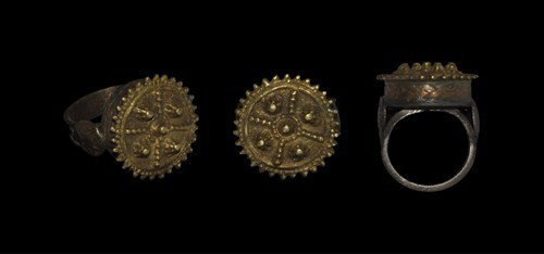 Byzantine - Filigree and Granule Finger Ring: Circa 10th century AD. A substantial finger ring comprising a cast flat-section hoop with running loop motif between everted edges; on the shoulders, two discoid panels with central boss and radiating