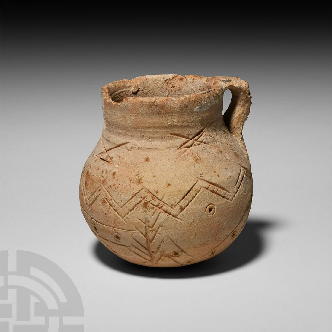 Syrian Incised Jug: 2nd-1st millennium B.C. A ceramic jug composed of a bulbous body, broad neck and integral strap handle decorated with incised crosshatching, circumferential bands of chevrons and stamped ring-and-dot