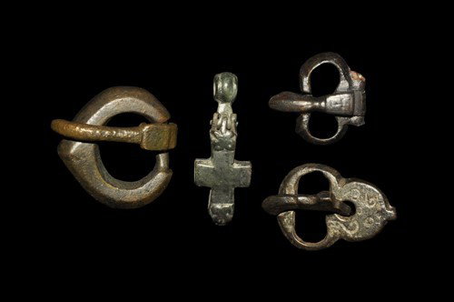 Byzantine Reliquary Pendant Cross and Buckles: Circa 6th-9th century AD. A group of cast bronze belt buckles comprising: one with heart-shaped loop and round-section tongue curved over the forward edge; one with kidney-shaped loop and clubbed tong