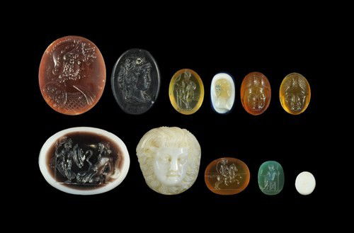 Roman Mixed Cameo and Intaglio Group: A mixed group of carved stone comprising: a blue and white cameo with female bust; an orange intaglio with horseman brandishing a kontos; a small white intaglio with a putto's face; a green intaglio w