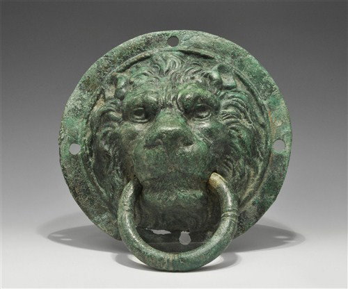 Roman Bronze Lion Mask Door Handle: Circa 2nd century AD A very large hollow cast bronze door handle formed as a lion mask within a circular frame; the mask stern with prominent brow and eyes, detailed mane framing the face; the sides o