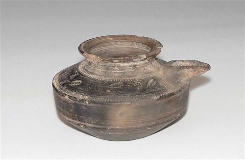 Islamic Ceramic Oil Lamp Filler: Circa 19th century AD or later A ceramic blackware vessel with discoid body, short spout, flat base and low neck; to the shoulder, concentric incised circles and billetted edges with a row of peacocks