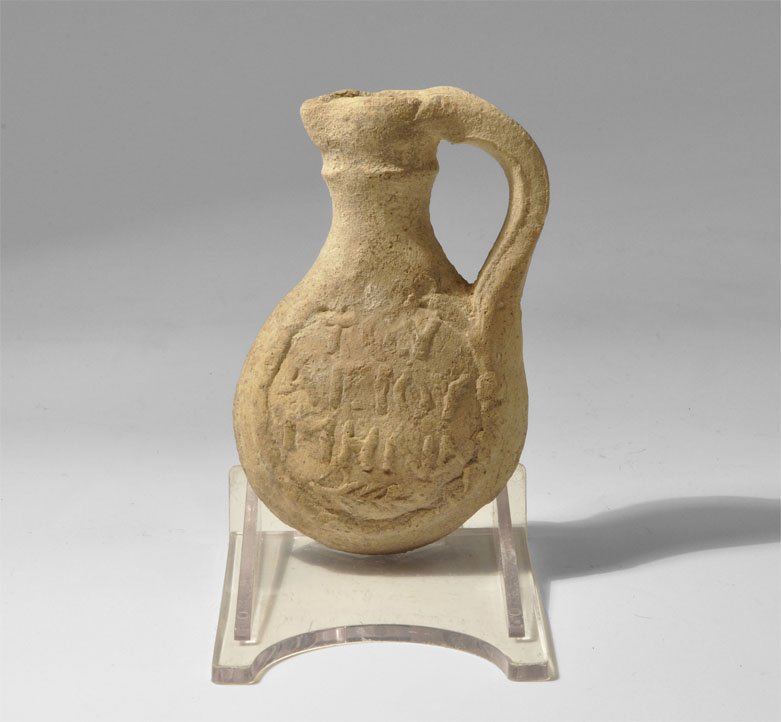 Byzantine Ceramic Inscribed St. Menos Pilgrim Flask: 8th-12th century AD. A Byzantine unglazed ceramic single-handled pilgrim's flask, one side with the Greek motto TOV ????? ???? (Saint Menas").above an olive branch, the other with a Greek cross of fol