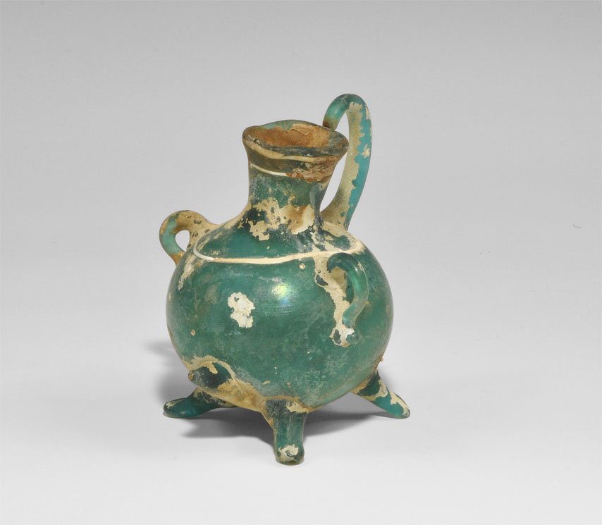 Islamic Green Glass Jug: An undated green glass jug: spherical body with four everted applied feet, two applied loop handles to either side of the body, applied scrolling handle to the neck, white trailed designs to body and 