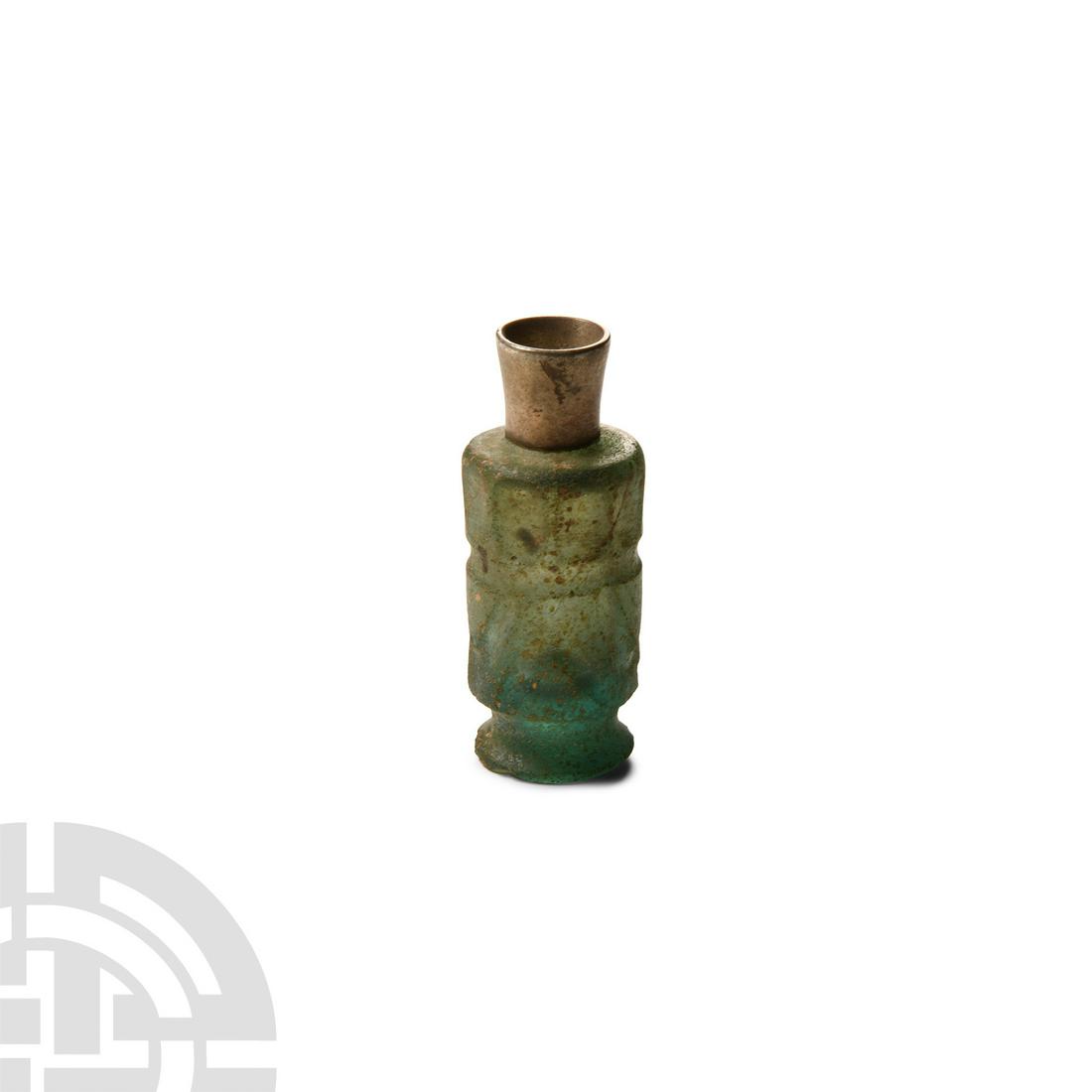 Western Asiatic Cut Glass Perfume Bottle with Silver Neck: 9th-11th century A.D. The bottle of cylindrical form with a foot, channel to the upper body with shallow rounded rectangular panels above and chevrons below; iridescent surfaces; later silver neck. 22