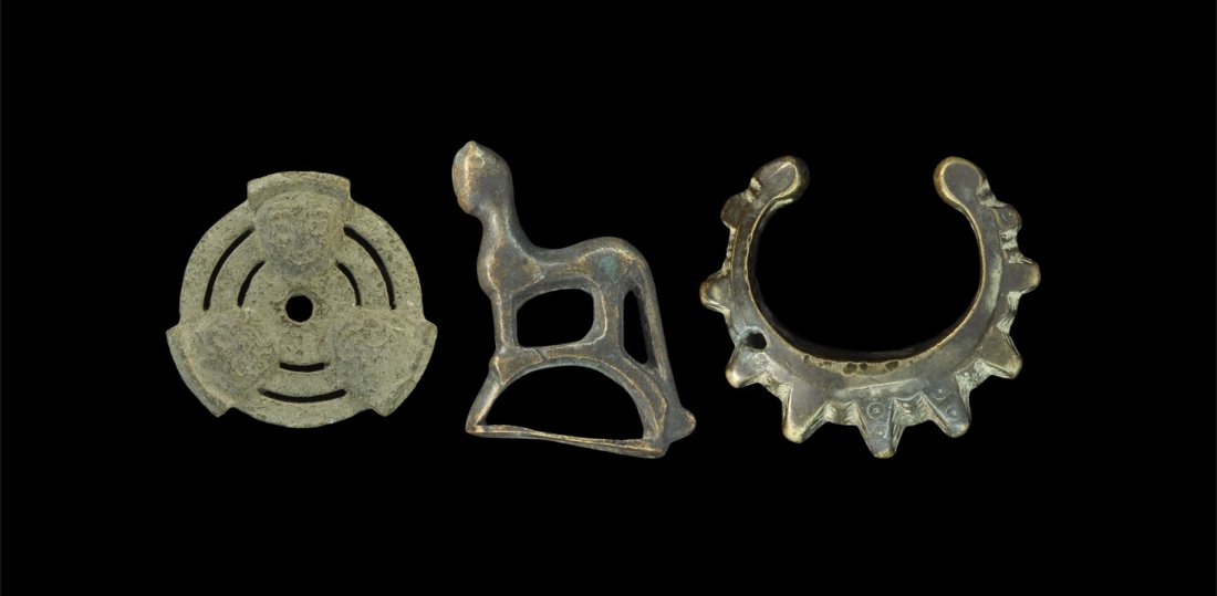 Near Eastern Bronze Figural Object Group: A mixed group of undated bronze items comprising: a cast lid formed from concentric rings and three D-shaped human masks; a stylised cat with D-shaped face on an arched base; a cast bracelet with radi