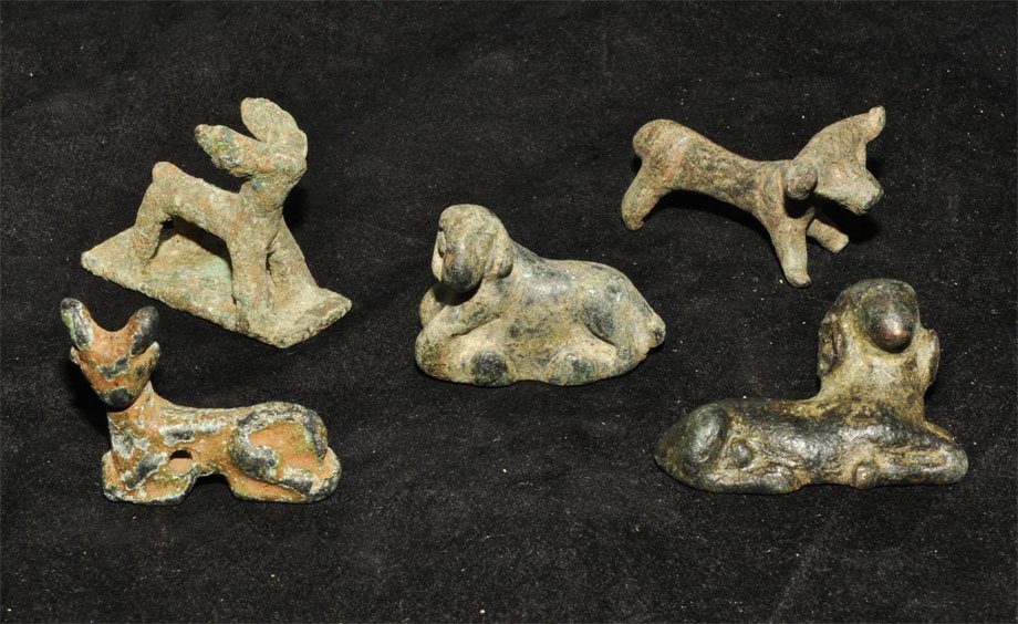Near Eastern Group of Animal Figurines: An undated group of five bronze zoomorphic figurines comprising a seated ram, a seated sheep, two standing bulls, one on a rectangular base, and a seated deer, pierced for suspension. Acquired on the 