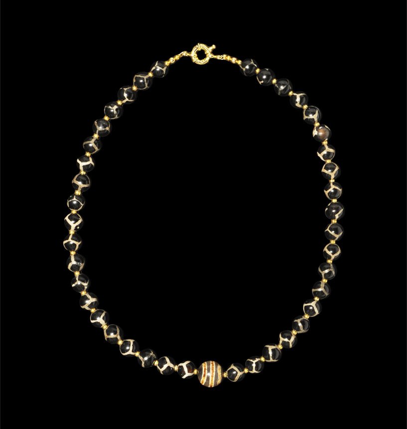 Islamic Pumtek and Agate Bead Group: Circa 19th century AD. A restrung necklace of globular pumtek beads and gold seed bead spacers; central globular banded agate bead; modern clasp. UK art market, acquired prior to 1985. 58 grams, 46 cm