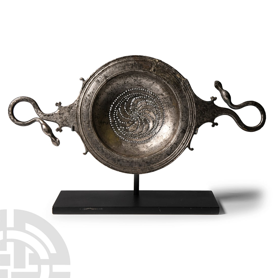 Greek Silver Wine Strainer: 4th-3rd century B.C. Composed of a shallow bowl and broad flange rim, two integral scalloped handles with scrolled flourishes, tapering to a loop handle with swan head terminals each with incised eye 