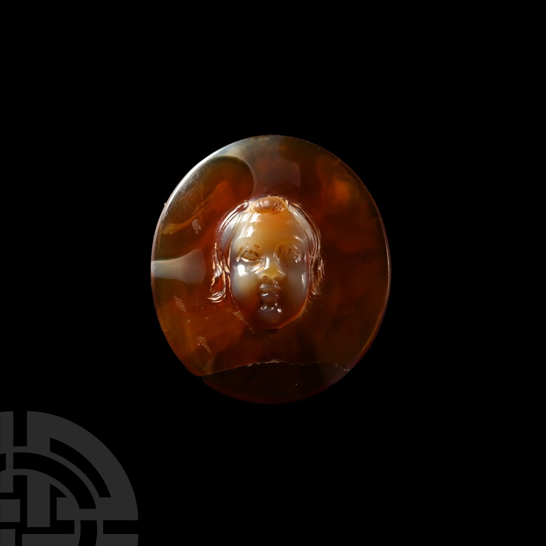 Roman Carnelian Cameo with Young Cupid: 1st-2nd century A.D. Lenticular-section disc with central recess to reverse; obverse with integral facing mask of Cupid modelled in the half-round; repaired. Cf. similar in green glass in the collecti