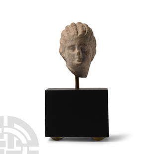 Greek Tanagra Terracotta Head of Aphrodite: Circa 4th-2nd century B.C. With hair divided in vertical arrangements, bound on the back by a fillet, delicate rendering of mouth, nose and eyes; mounted on a custom-made display stand. Cf. Mavrogonat