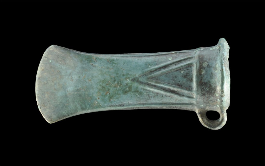 Bronze Age Decorated Looped and Socketed Axe Head: Middle European, circa 800-500 BC. A cast looped and socketted axe head with flared edge, collar to mouth and raised V-shaped rib to each face. Property of a European Gentleman living in the UK; ex pr