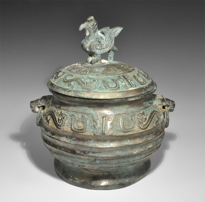 Chinese Style Large Bronze Lidded Vessel: An undated bronze vessel with lid; the vessel with fluted ribs to the body, low base and everted rim, to the shoulder a band of zoomorphic ornament reserved against a textured field and two beast-head