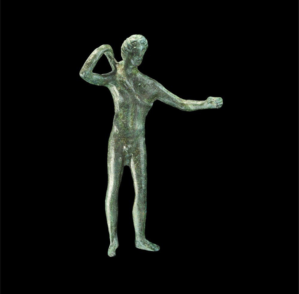 Roman Style Bronze Apollo Statuette: An undated cast bronze figurine representing a nude Apollo with curled hair and slender build in 1st-3rd century AD style; the left arm extended holding a bow (lost in antiquity) and the right hand re