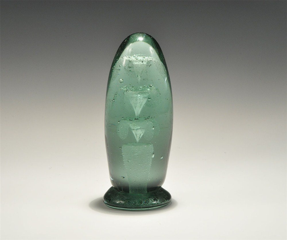 Post Medieval Victorian Glass Paperweight: 19th century AD. A green glass amphora-shaped fairing paperweight with three-tier fountain motif; of naive manufacture. Glass, 892 grams, 15.5 cm (6"). Ex Douglas Rose Collection. [No Reserve]
