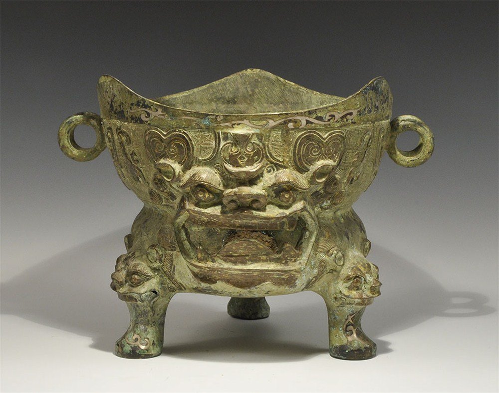 Chinese Style Large Bronze Figural Vessel: An undated cast bronze vessel with hollow tripod legs and double-loops; the legs with beast-head detail to the knee; the body with globular bowl and dished upper section, decorated with inlaid silver 