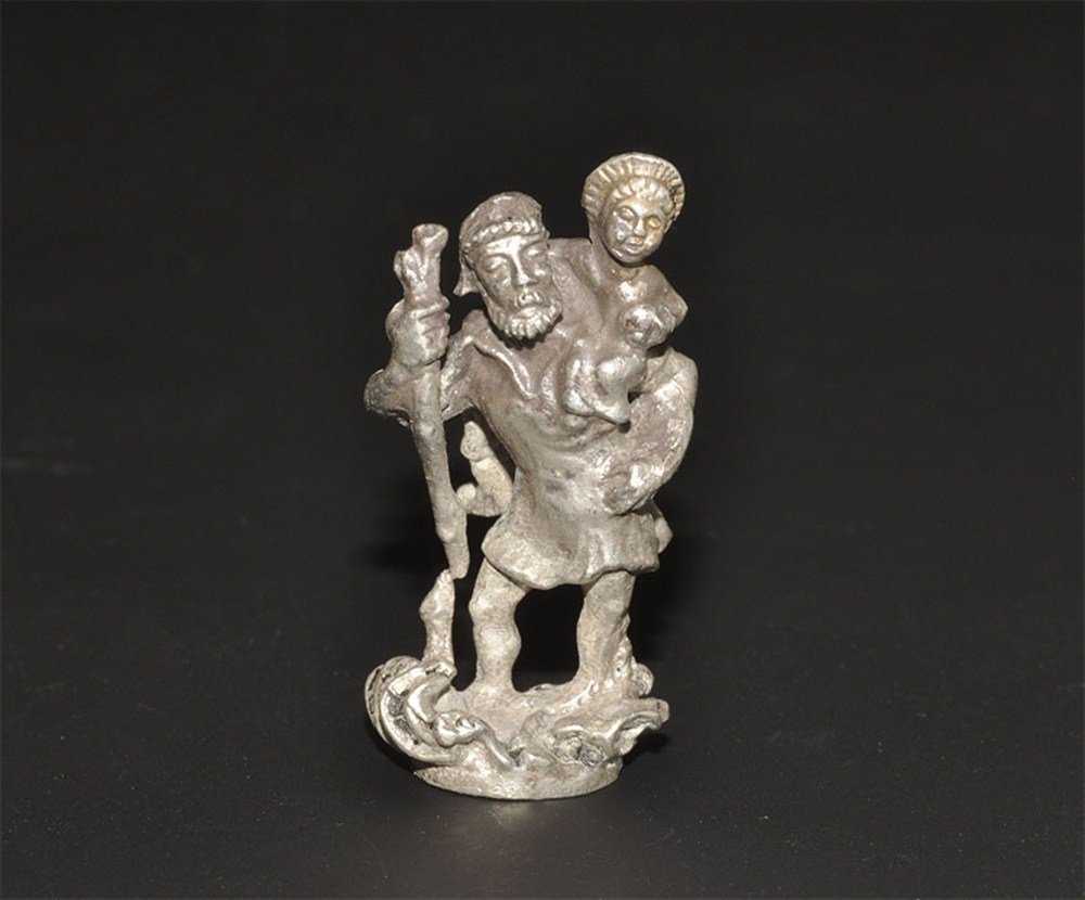 Post Medieval Silver St Christopher Figurine: 19th century or later. A cast silver figurine depicting St Christopher in a loose tunic and cloak wading in scrolled waves, supporting himself with a staff in his right hand, carrying the nimbate baby