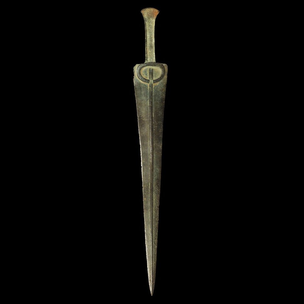 Near Eastern Luristan Bronze Short Sword: Bronze Age, 1250-650 BC A cast short sword comprising a triangular blade with lentoid-section midrib and raised penannular block to the upper end; the grip flat with flanges to the edges to accept org