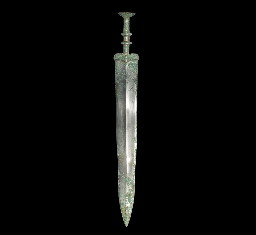 Chinese Bronze Short Sword: Han Dynasty, 206 BC-220 AD A cast tin-rich sword with gently tapering blade, slightly waisted; the hilt columnar with two flanges to the grip and larger concave flange pommel above; the guard lentoid 