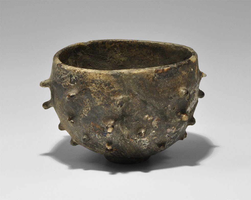 Islamic Syrian Glass Spiked Bowl: 7th-8th century AD A dark hemispherical bowl with discoid base, the outer face with rows of short decorative spikes. Cf. Newark Museum Catalogue, items 233 and 524-6 for similar. 165 grams, 10 cm. (4"