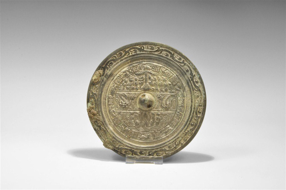Chinese Bronze Mirror with Figural Motifs: Han Dynasty, 206 BC-220 AD A cast disc mirror with one polished surface; to the reverse, a pierced central boss surrounded by a field divided into three zones showing four figures and serpents, two zo