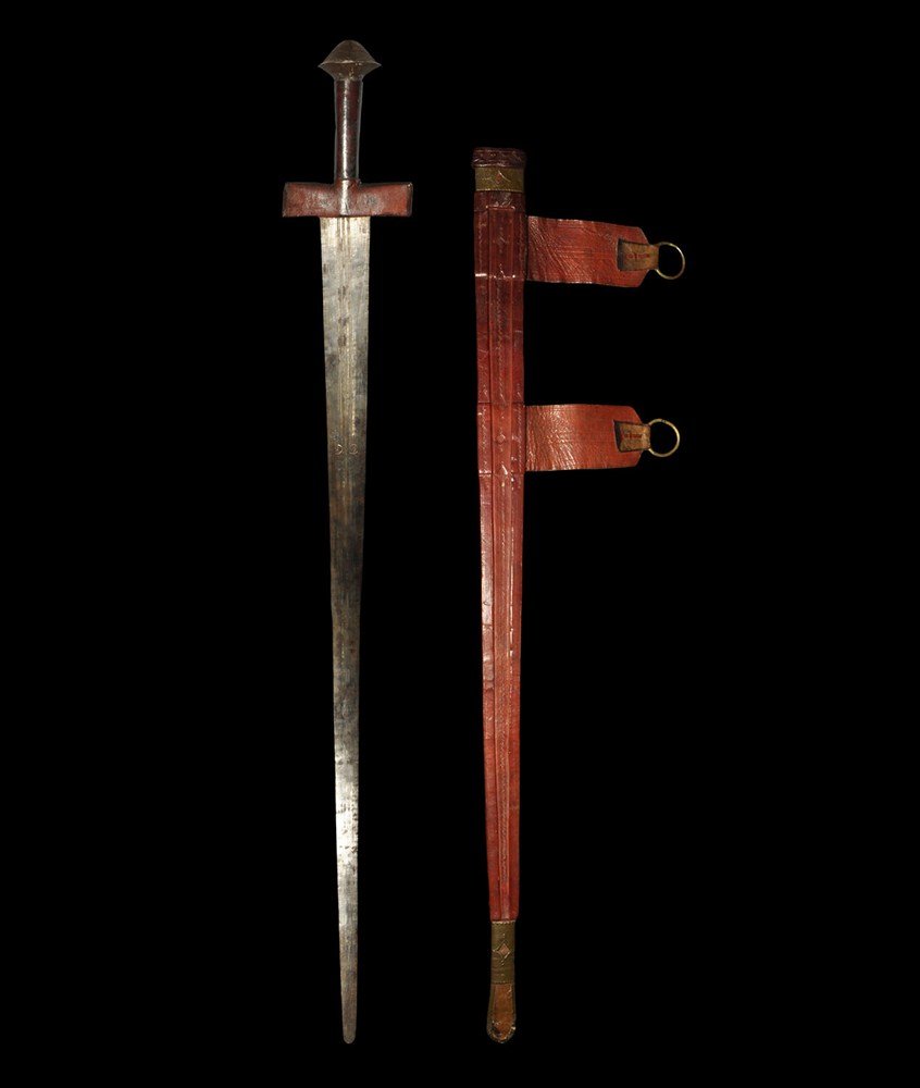 Post Medieval Dervish Sword & Scabbard: Circa 19th century AD. A two-edged sword with slender triangular blade, leather quillons, tubular grip and discoid pommel with pyramidal upper face; the blade with three shallow fullers, knurled bandi