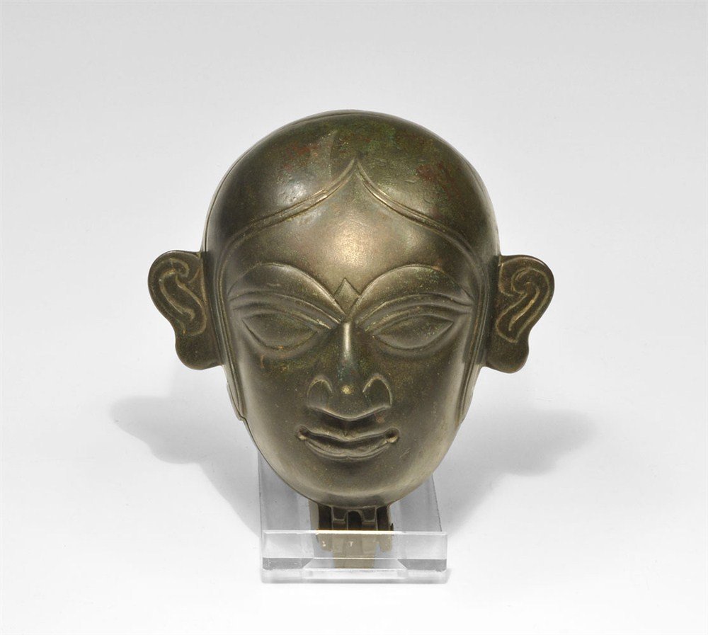 Indian Bronze Hinged Figural Box: Circa 19th century AD. A cast bronze container in the form of a human head mask, hinged beneath the chin; the face with lentoid eyes, scrolled ears and recesses to the corners of the mouth. Acquired o